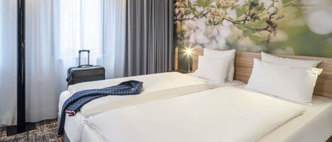 A hotel room with a large bed, a bedside table, a lamp, and a window with curtains.
