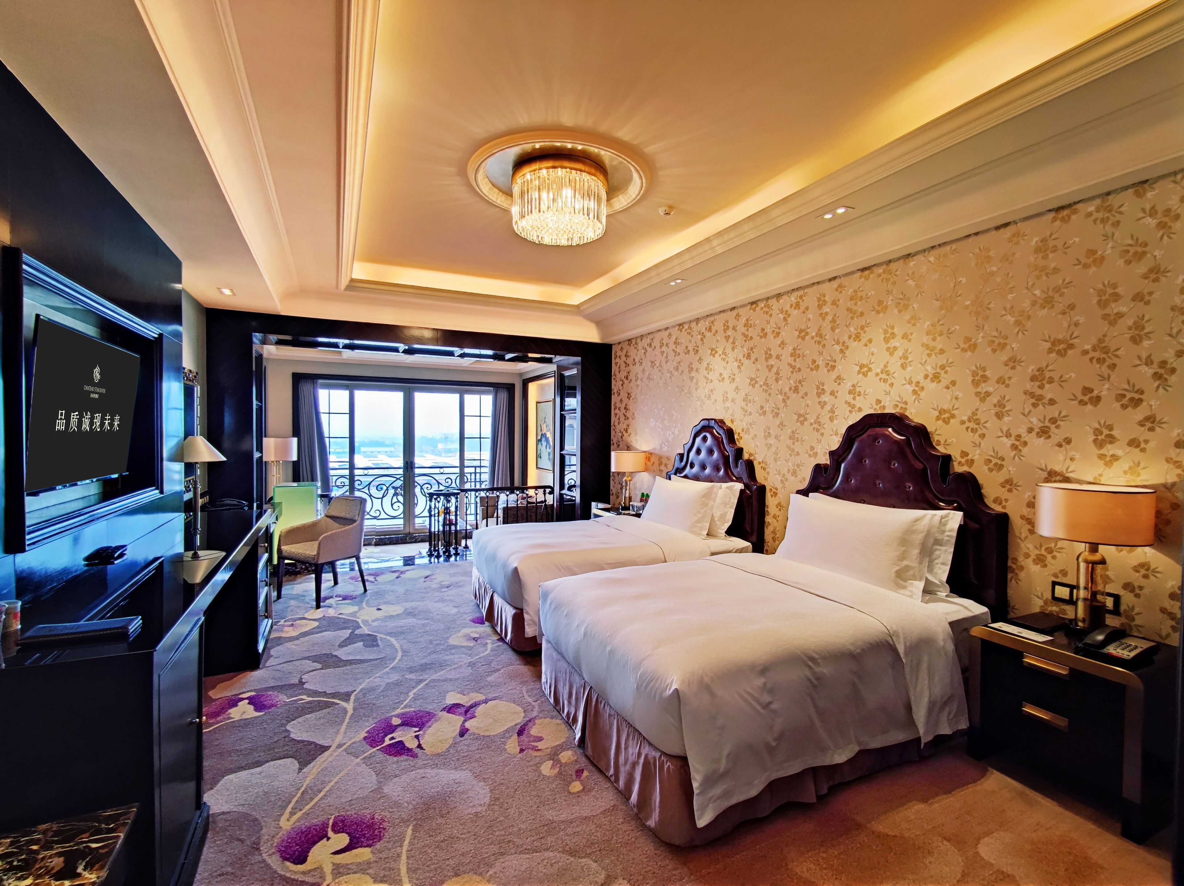 A hotel room with two beds, a television, a desk, and a balcony with a view.