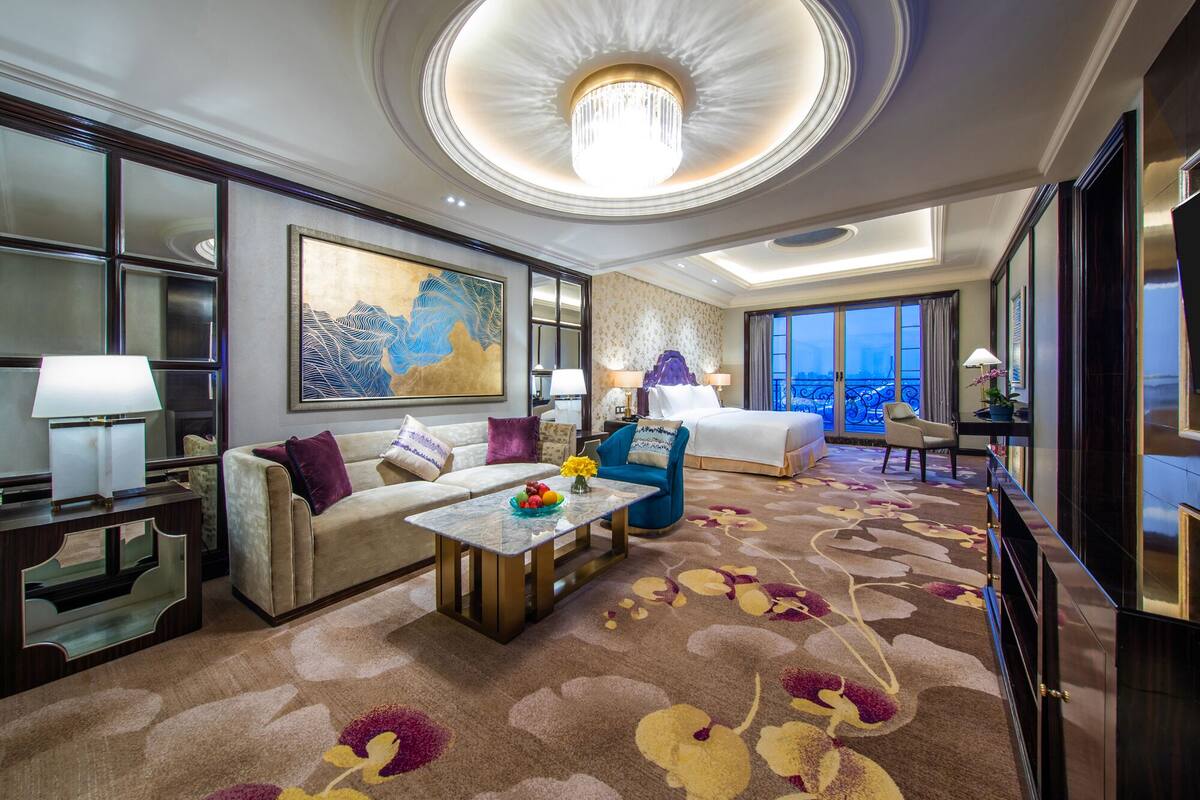 Une chambre d’hôtel spacieuse, dotée d’un grand lit, d’un canapé, d’une table basse et offrant une vue sur le paysage urbain.