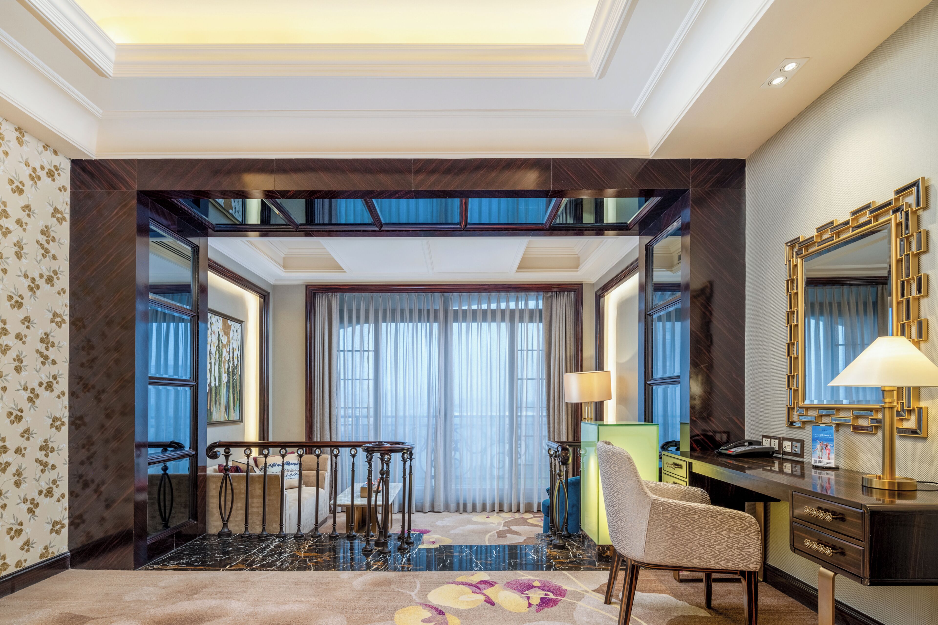 A hotel room with a large mirror, a desk, a chair, a bed, and a view of the city through large windows.