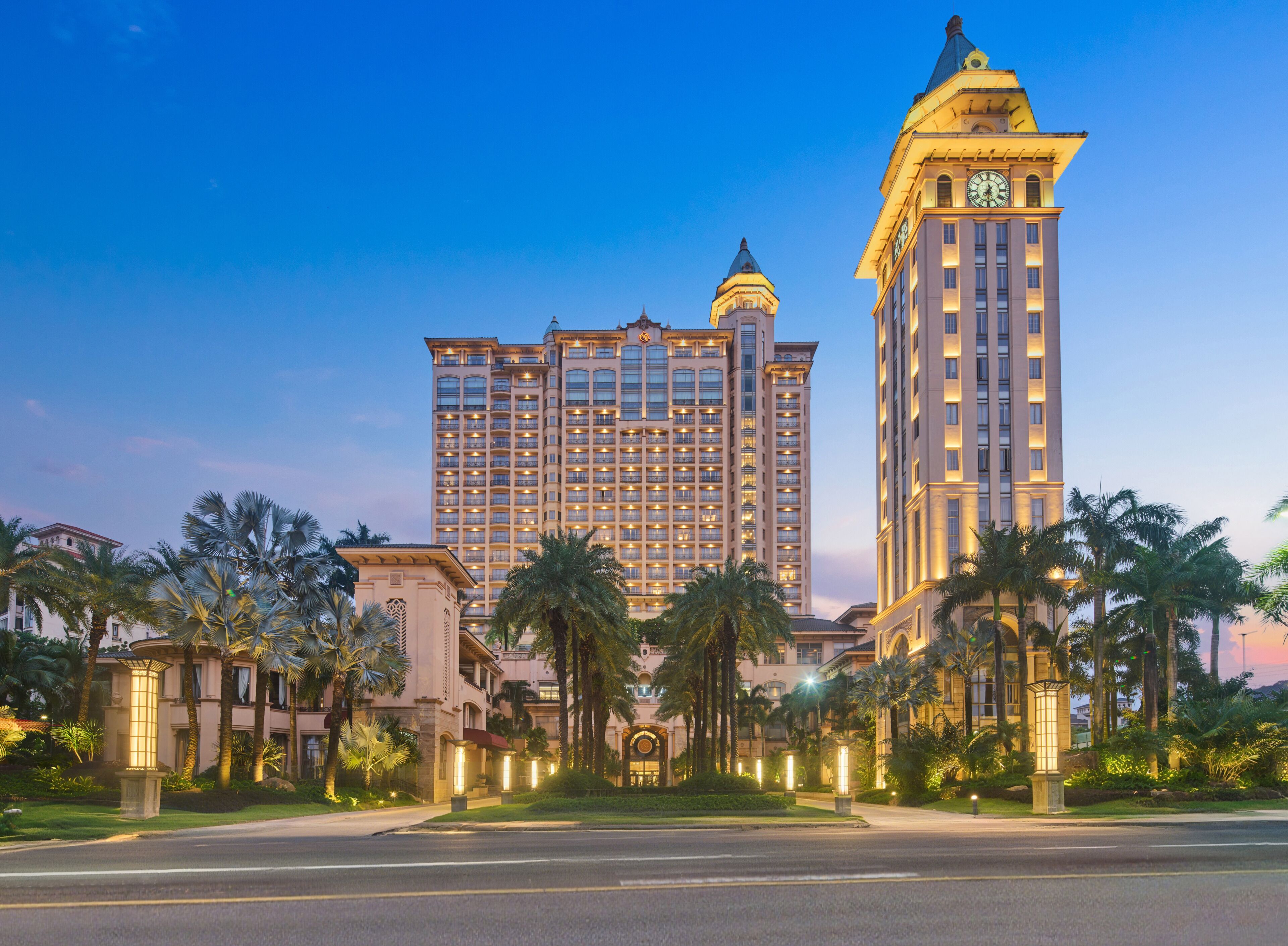 A large hotel with multiple floors, a prominent clock tower, and palm trees in the foreground.