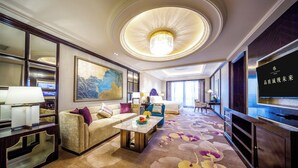 A spacious hotel room with a large bed, a sitting area with a sofa and armchairs, a dining table, and a television. - Chateau Star River Guangzhou (Guangzhou)