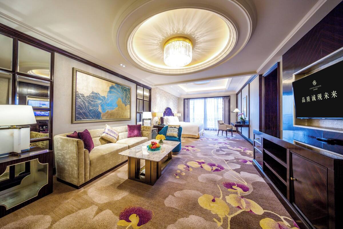 Une chambre d’hôtel spacieuse, dotée d’un grand lit, d’un coin salon avec un canapé et des fauteuils, d’une table à manger et d’un téléviseur.