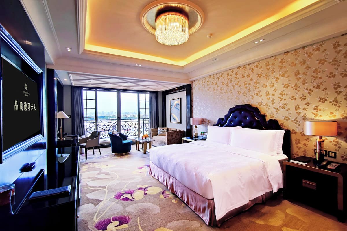 Une chambre d’hôtel avec un grand lit, un bureau, une chaise, une télévision et un balcon donnant sur la ville.
