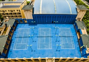 Un court de tennis comprenant quatre terrains, entouré de bâtiments dotés d’un toit bleu et de murs de couleur beige.