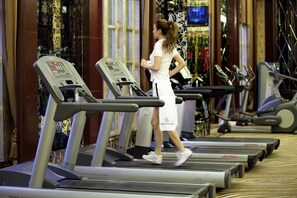 Une femme marche sur un tapis de course dans une salle de sport où plusieurs tapis de course sont alignés.