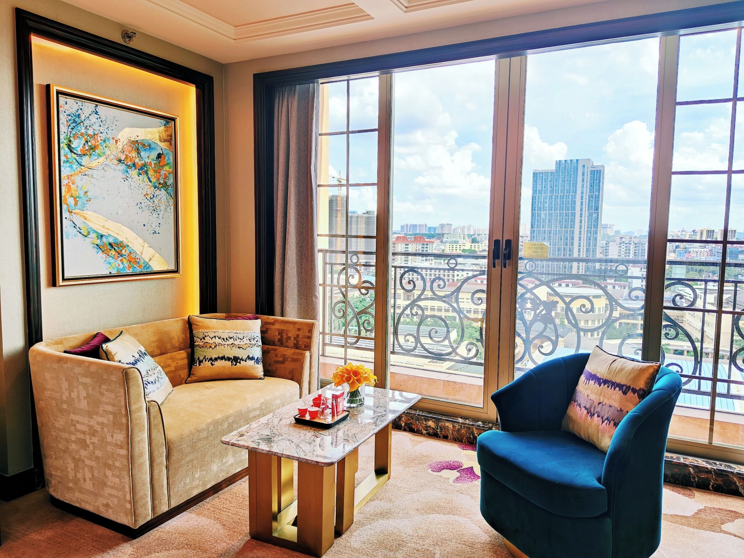 A living room with a sofa, a blue armchair, a coffee table, and a large window with a view of buildings.