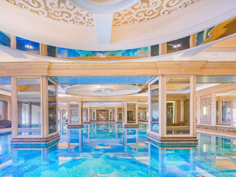 A large indoor swimming pool with a tiled floor and a high ceiling with ornate decorations.