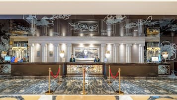 Ein Hotel-Empfangsbereich mit Marmorböden, einem Empfangstresen und dekorativer Wandgestaltung.