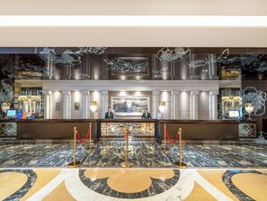 Ein Hotel-Empfangsbereich mit Marmorböden, einem Empfangstresen und dekorativer Wandgestaltung.