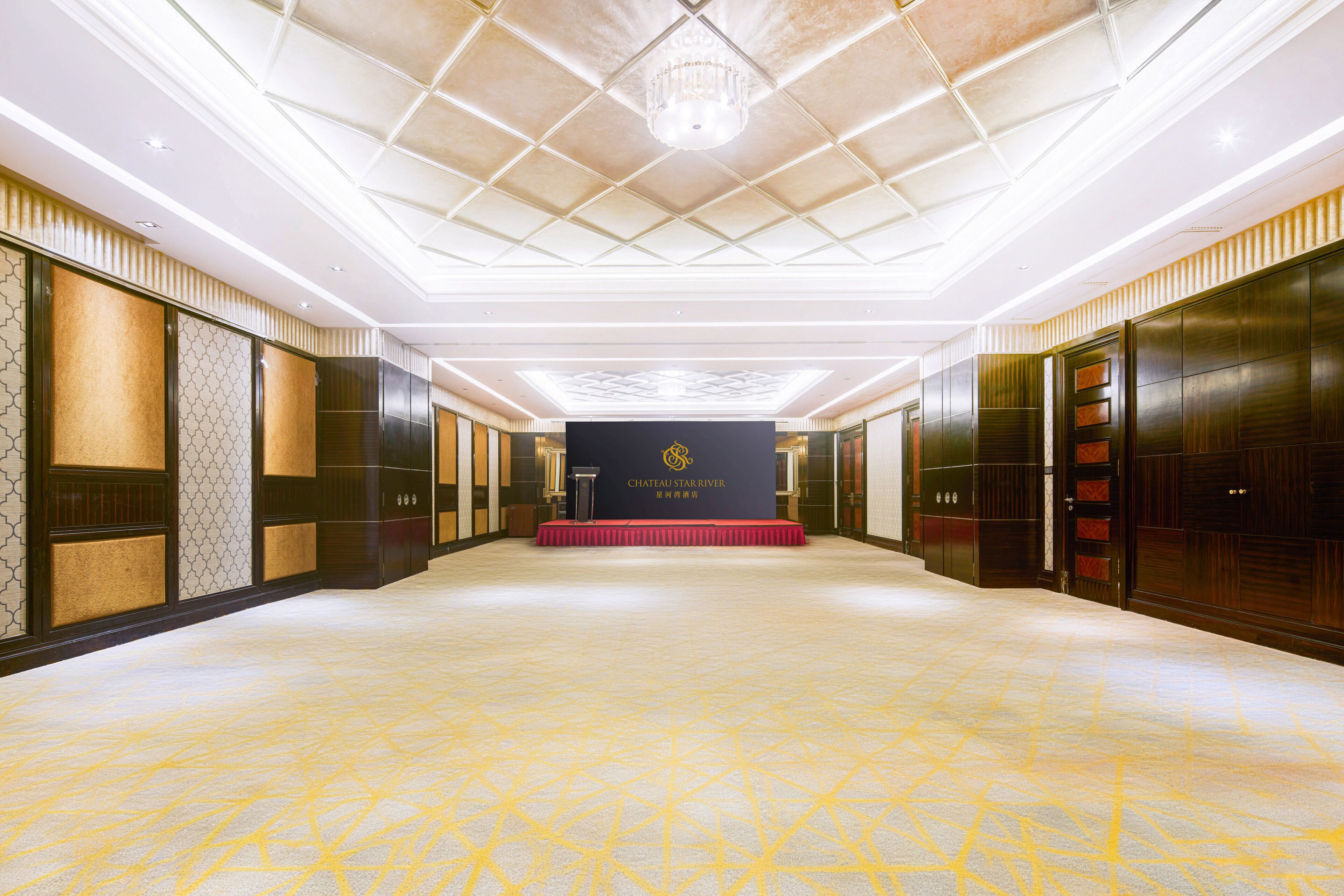 A hotel lobby with a central stage, dark wood paneling, and a patterned floor.