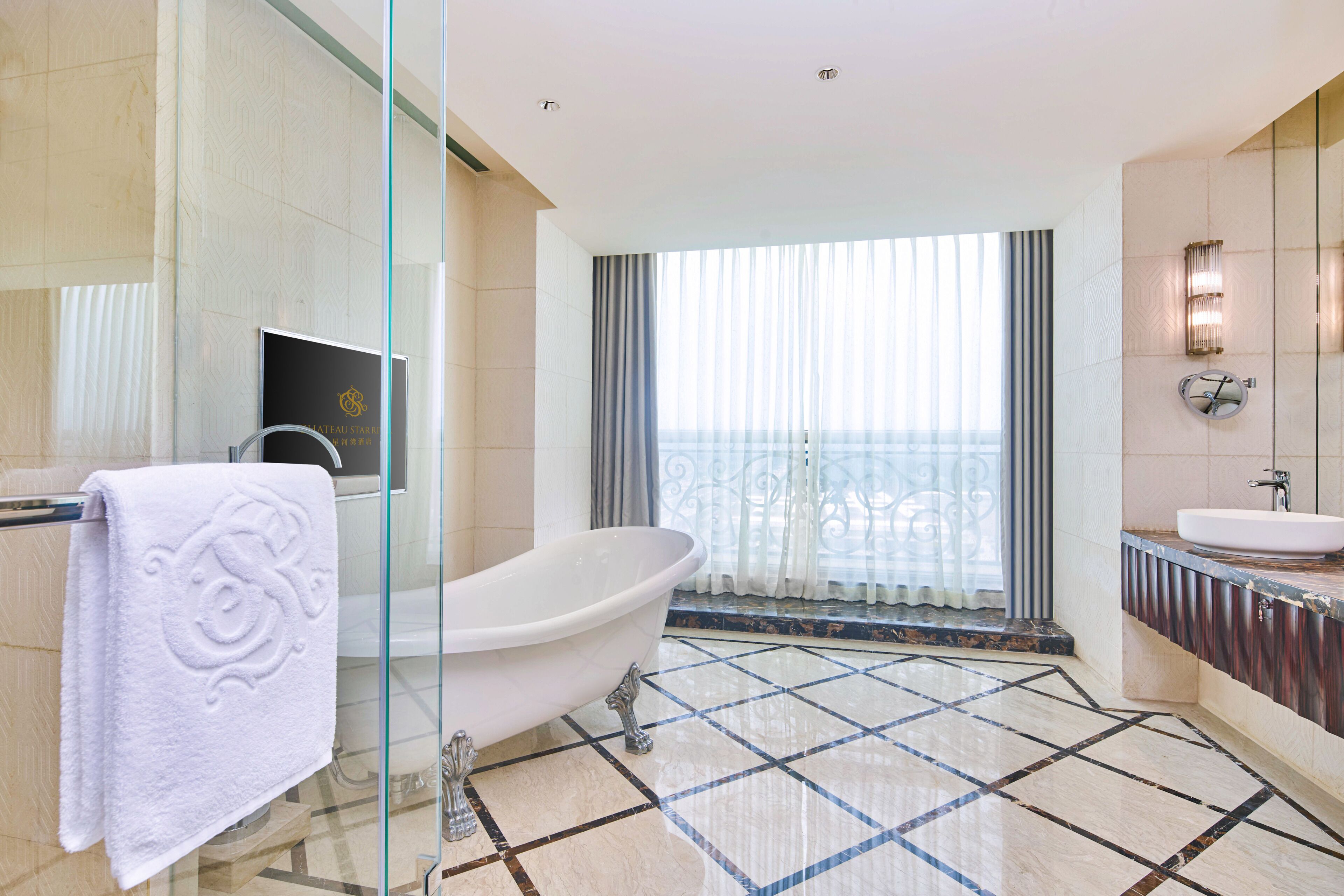 A modern bathroom with a freestanding bathtub, a vanity with a sink, and a large window offering a view of the sea.