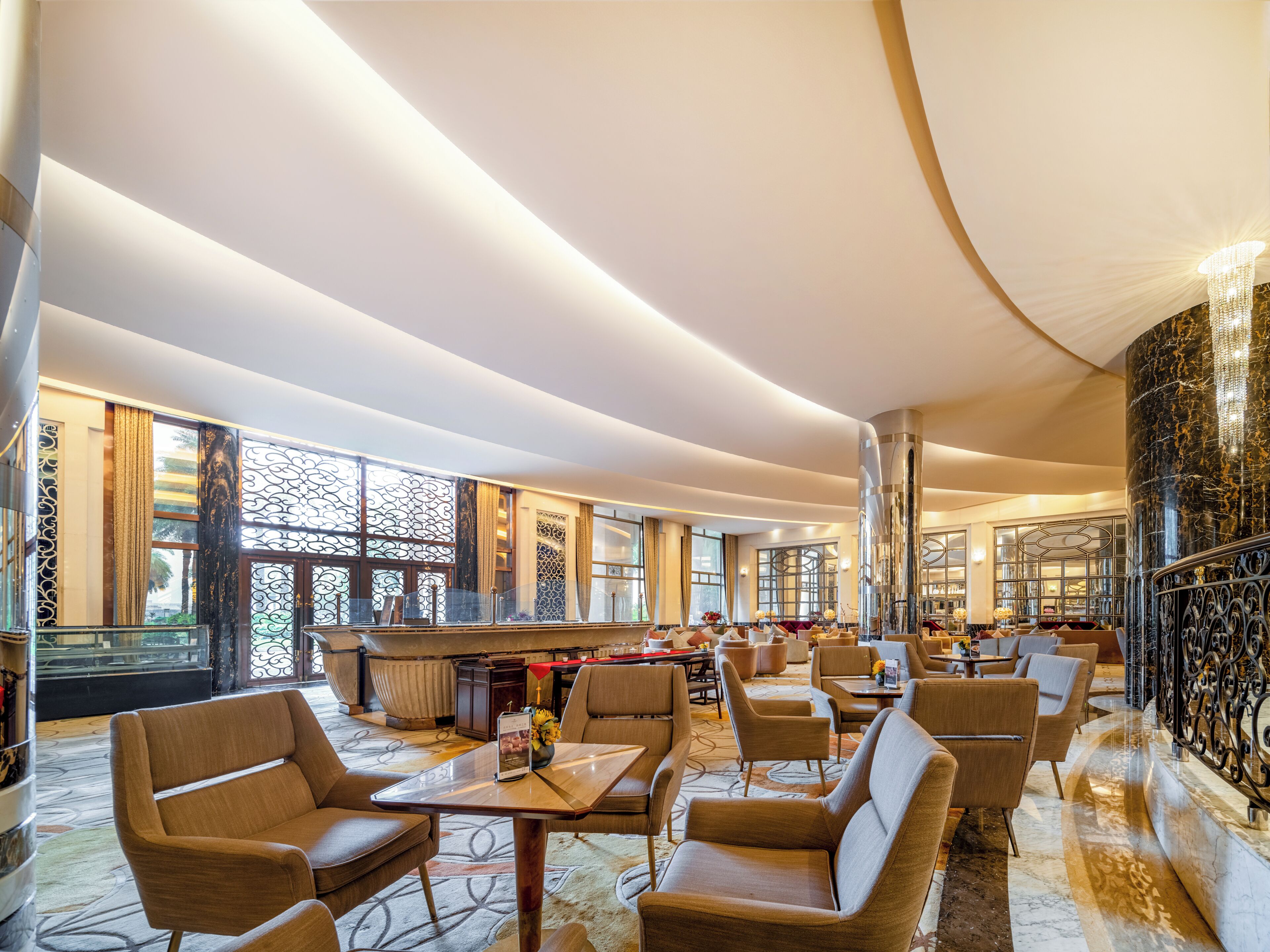 Un amplio vestíbulo de hotel con techos altos, grandes ventanales y mobiliario moderno.