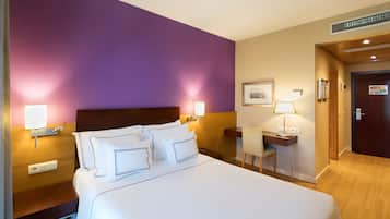 Una habitación de hotel con una cama grande, mesitas de noche con lámparas, un escritorio y una silla.