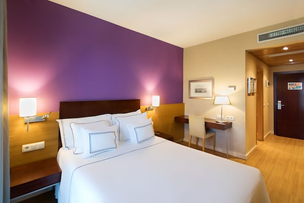 Una habitación de hotel con una cama grande, mesitas de noche con lámparas, un escritorio y una silla.