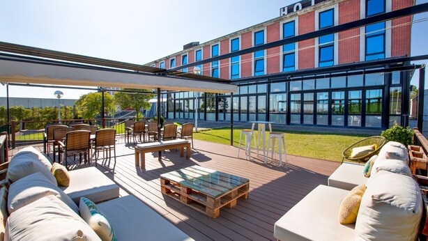 A hotel patio with outdoor seating, a glass-enclosed building in the background, and a clear view of the surrounding area. - AZZ Salamanca Montalvo (Salamanca)