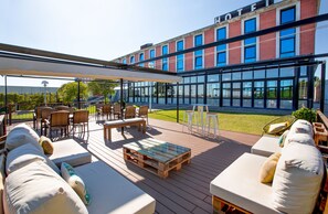 A hotel patio with outdoor seating, a glass-enclosed building in the background, and a clear view of the surrounding area. - AZZ Salamanca Montalvo (Salamanca)