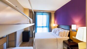Een hotelkamer met een stapelbed, een nachtkastje met een lamp, een bureau en een raam met gordijnen.