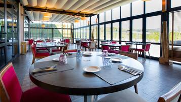 Un restaurante con mesas redondas, sillas rojas y amplios ventanales con vistas.