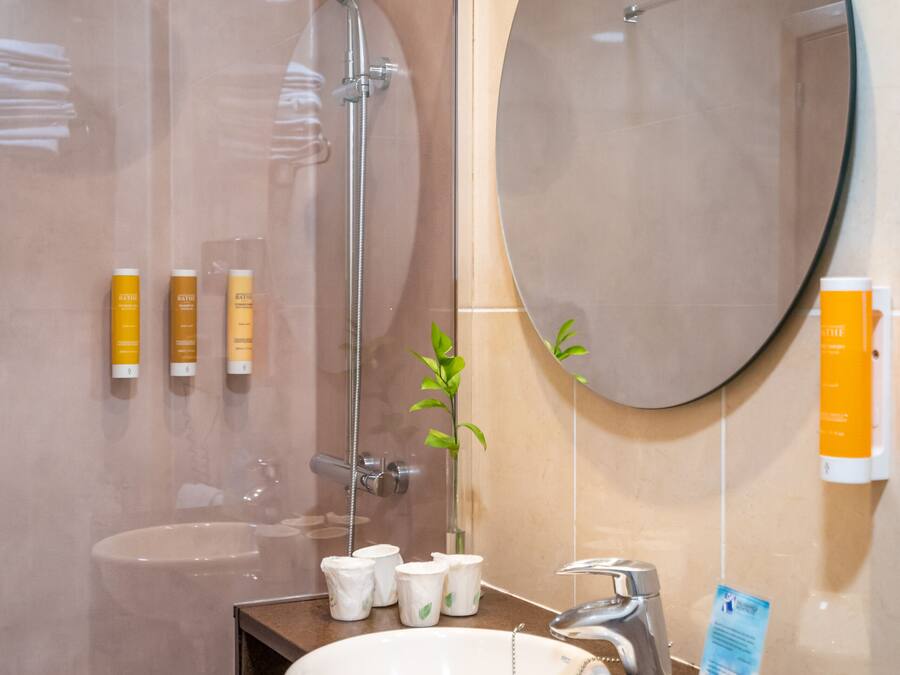 Une salle de bain avec une douche à parois de verre, un lavabo avec un miroir au-dessus et des articles de toilette fixés au mur.