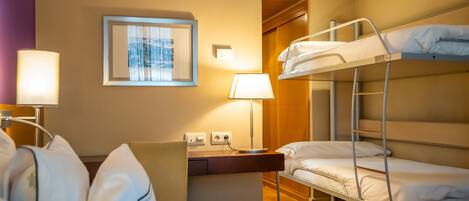 A hotel room with bunk beds, a desk, a chair, a lamp, and a framed picture on the wall.