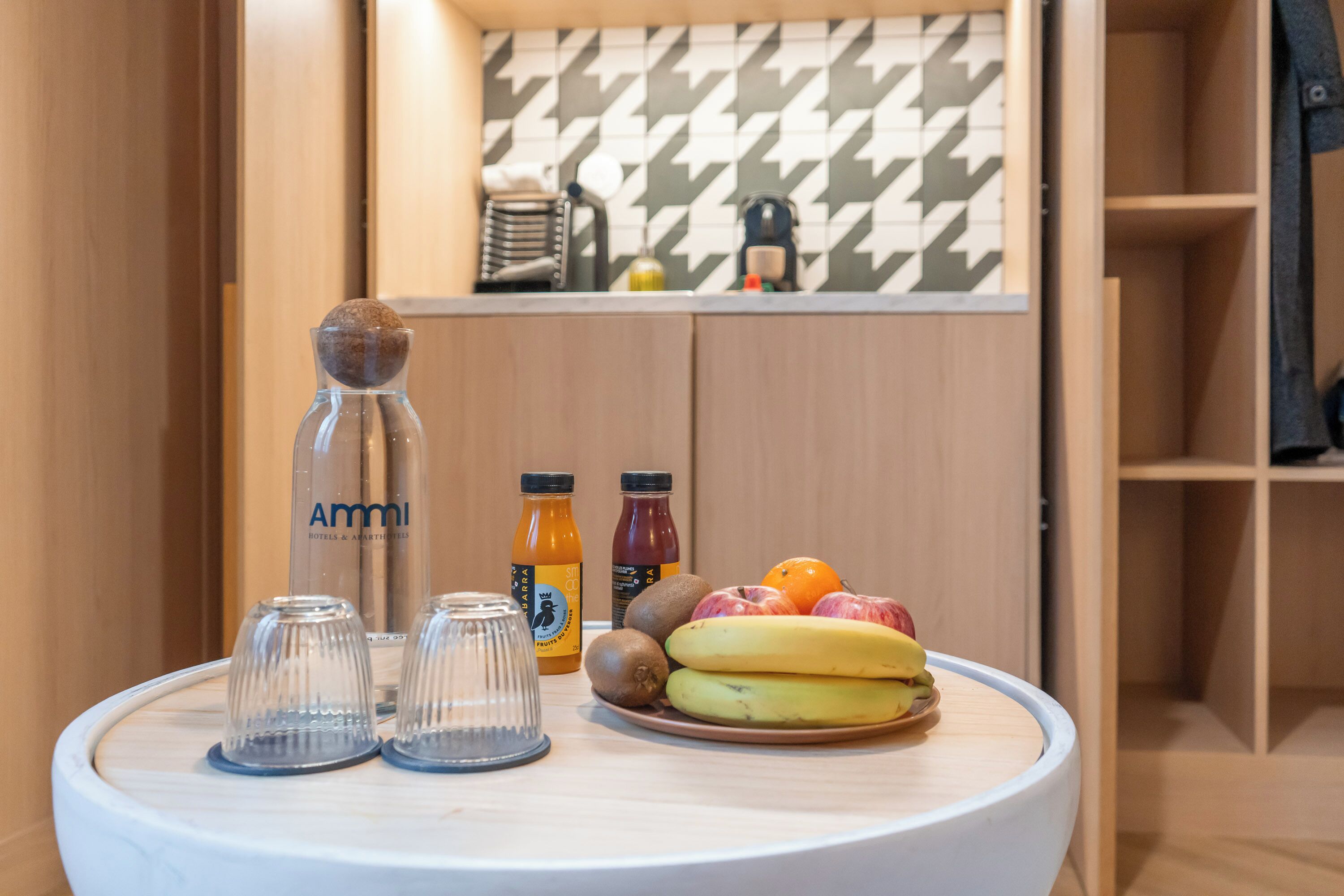 Una mesa pequeña con un plato de fruta, dos botellas de jugo y una jarrón con agua.
