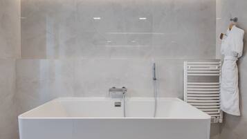 Un baño moderno con una bañera grande, un perchero para toallas y un calentador de pared.