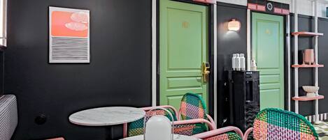 A hotel room with a black and green color scheme, featuring a round table with a white marble top, colorful woven chairs, and a framed picture on the wall.
