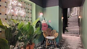 A hallway with a neon sign, potted plants, a wicker chair, and a staircase. - Hotel Aparthotel AMMI Nice Lafayette (Nice)