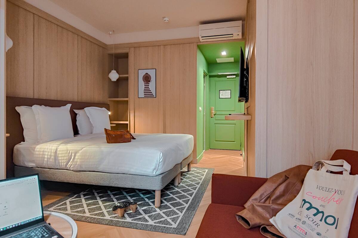 Una habitación de hotel con una cama, una computadora portátil, un bolso de mano y una bolsa de tela en el suelo.