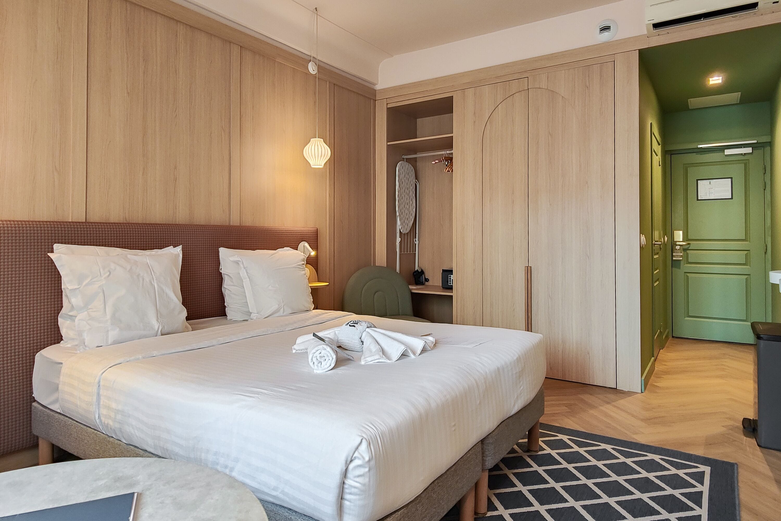 A hotel room with a large bed, a desk, a chair, and a wardrobe.