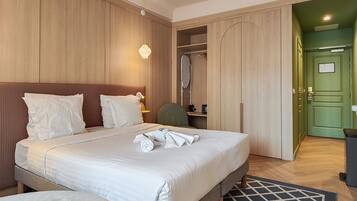 A hotel room with a large bed, a desk, a chair, and a wardrobe.