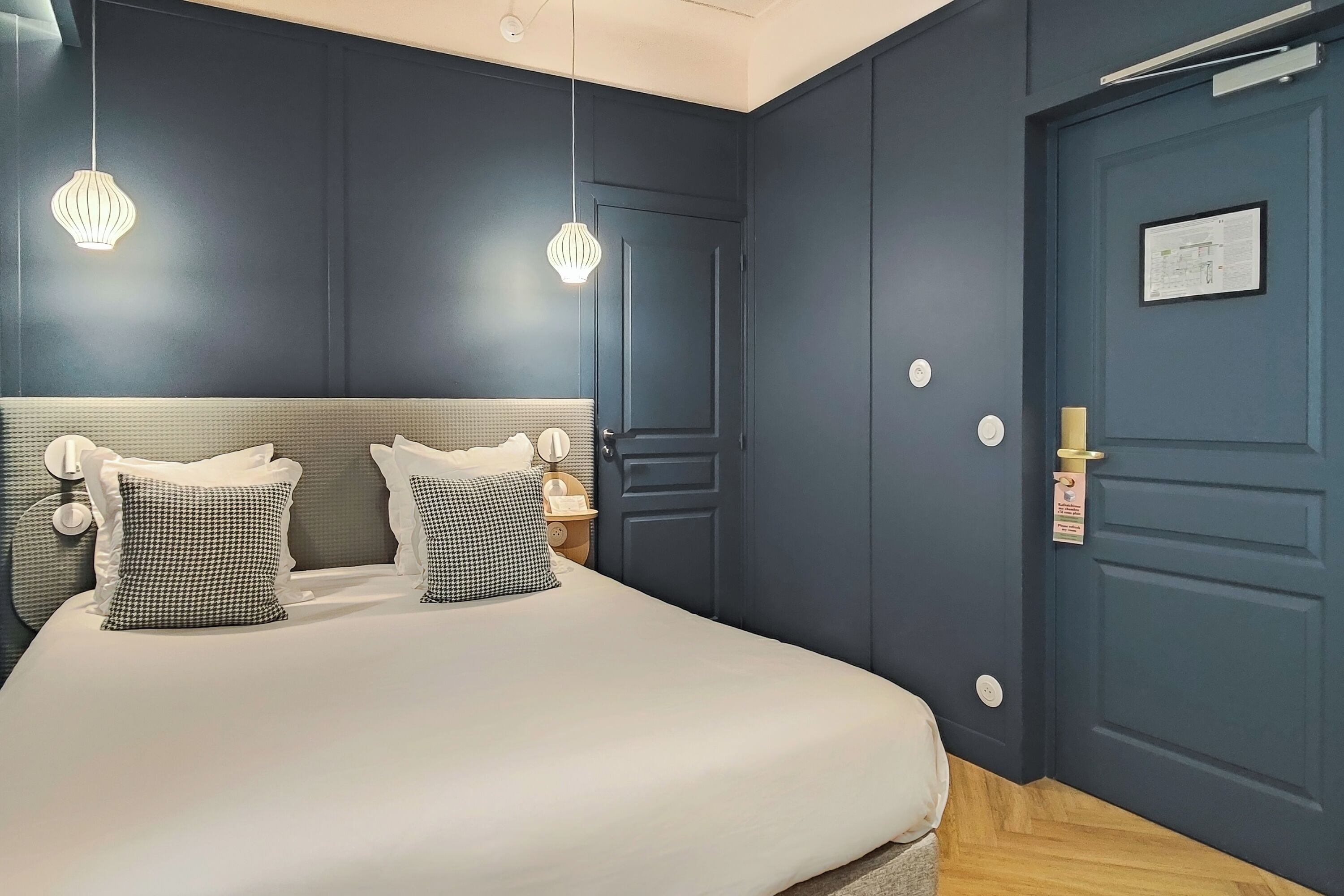 Un dormitorio con una cama grande, dos mesitas de noche, un tocador, una puerta azul oscuro y una lámpara.