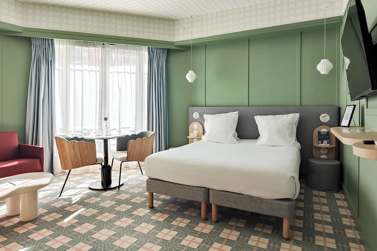 Habitación de hotel con una cama grande, un escritorio con sillas, un sofá rojo y un televisor montado en la pared.