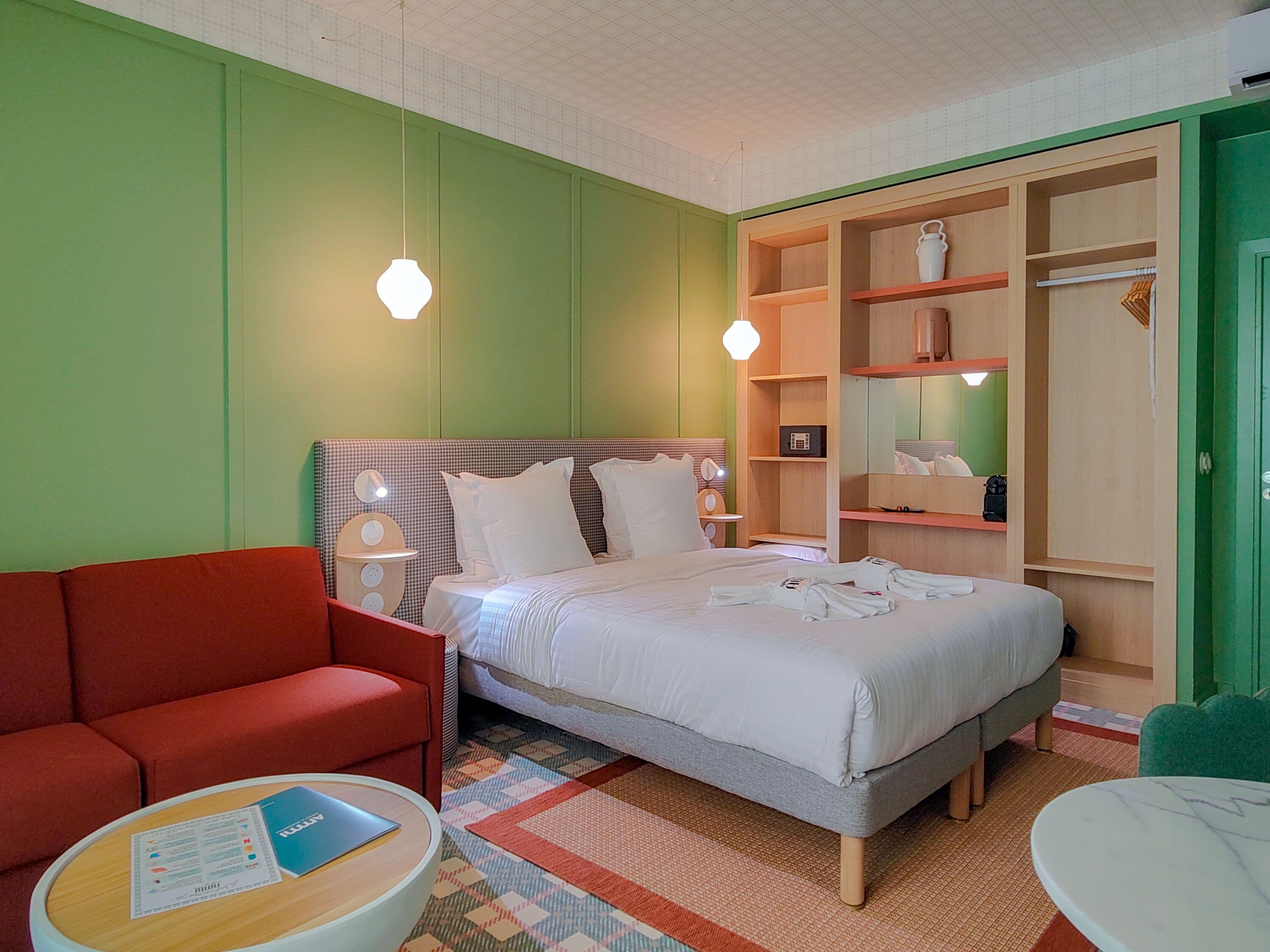 Una habitación de hotel con una cama, un sofá rojo, una mesita redonda con un menú y un armario verde.