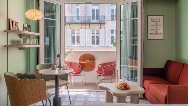 A hotel room with a balcony, a round table, red chairs, a sofa, and a bed. - Hotel Aparthotel AMMI Nice Lafayette (Nice)