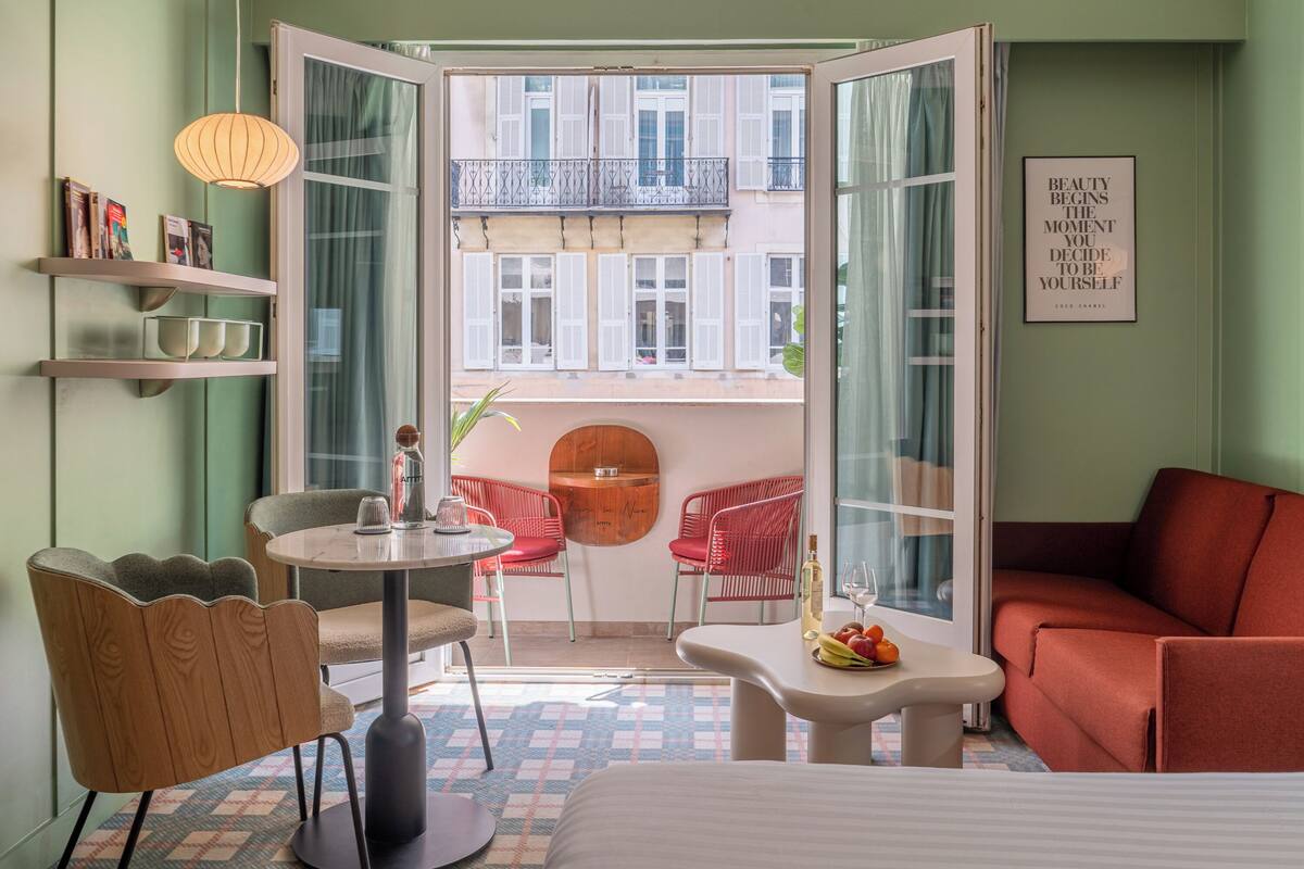 Habitación de hotel con balcón, una mesa redonda, sillas rojas, sofá y cama.