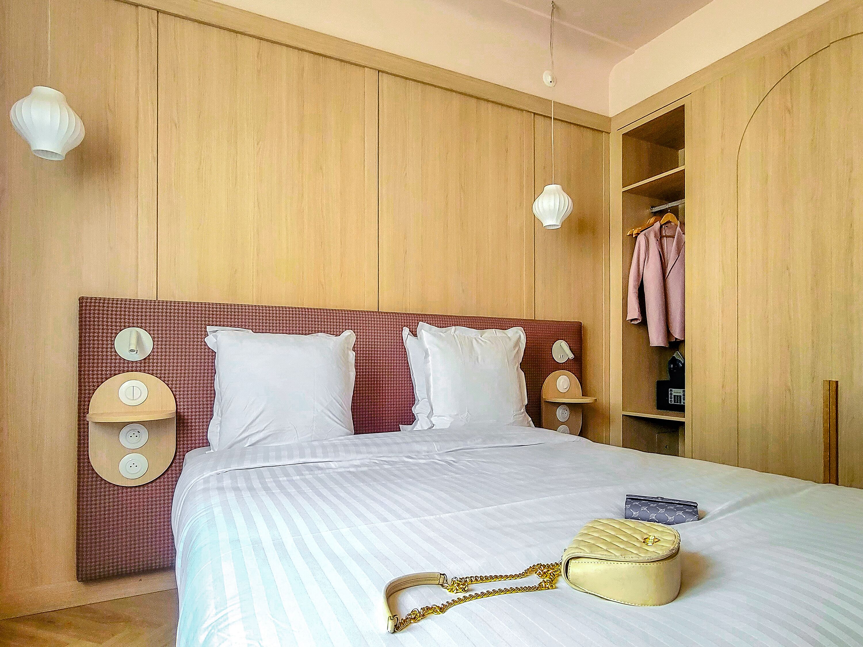 A hotel room with a large bed, wooden panel walls, a wardrobe, and a bedside table with a lamp.