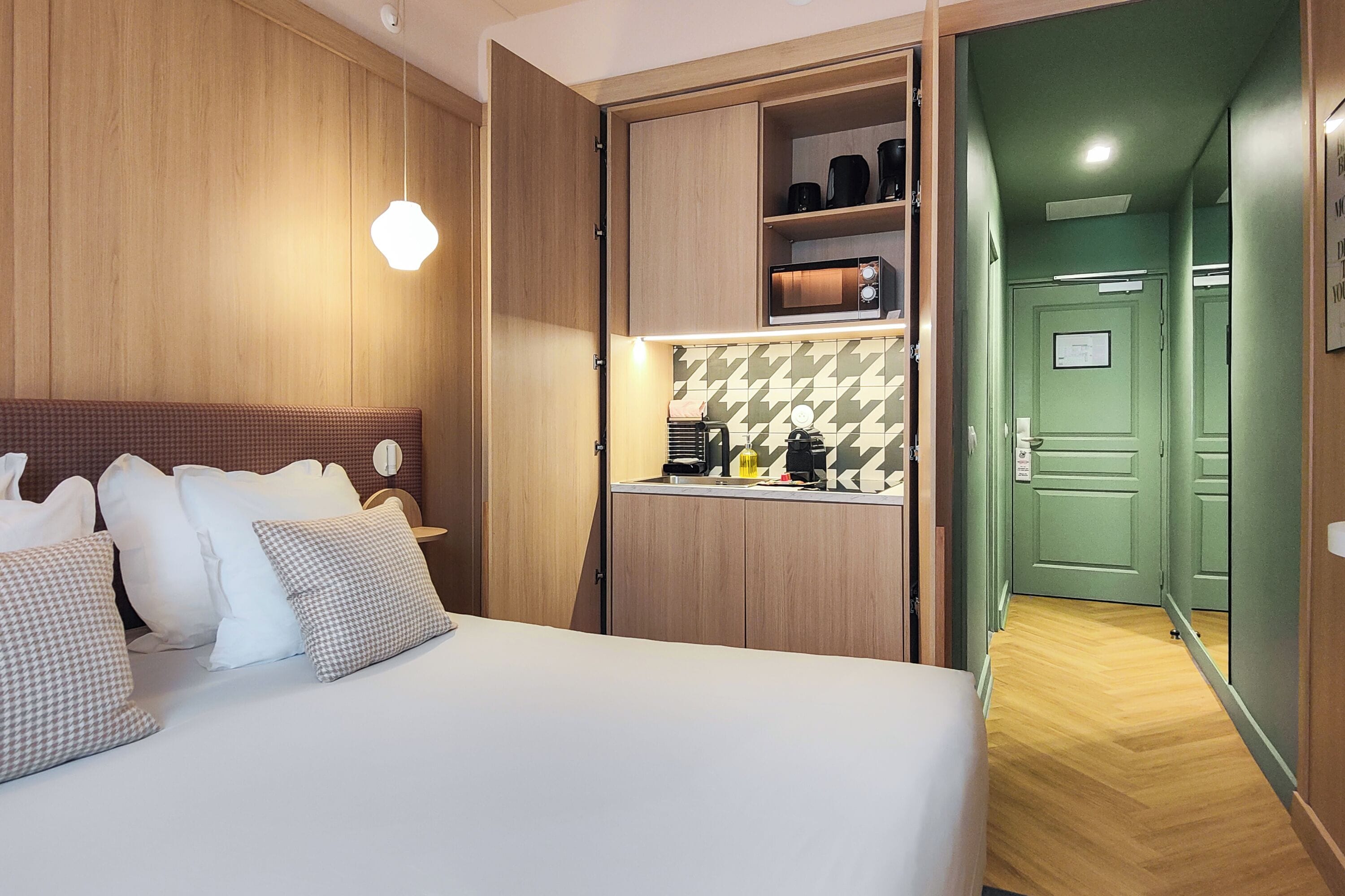 A hotel room with a bed, a kitchenette, and a green door.