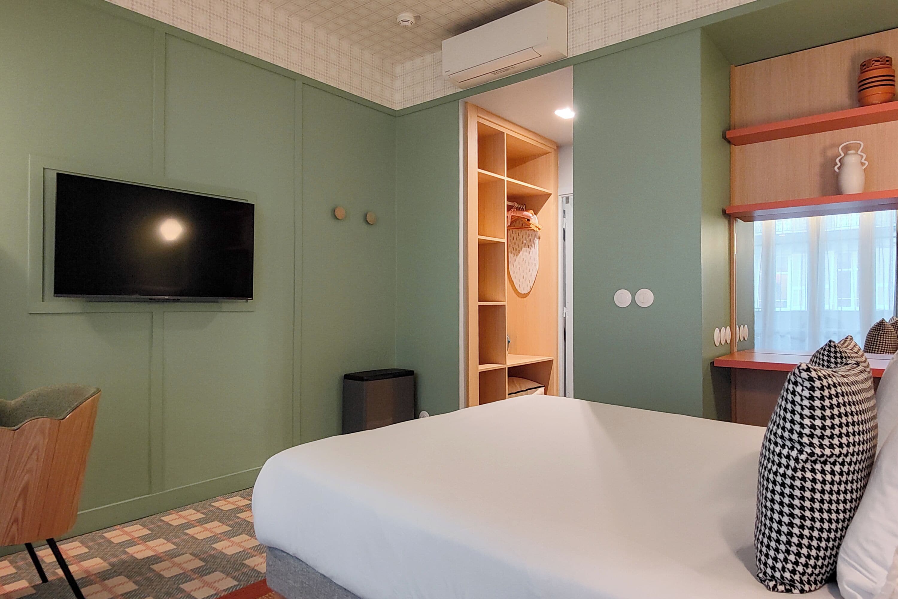 A bedroom with a bed, a television, a wardrobe, and a window with curtains.