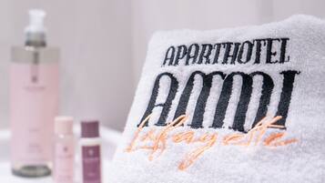 Una toalla con bordado que dice "APARTHOTEL AMO" y "Lafayette" en un entorno hotelero.