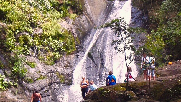 Ein Wasserfall, umgeben von üppiger Vegetation, während Menschen die natürliche Umgebung genießen.