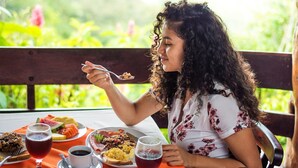 Uma pessoa jantando em uma mesa ao ar livre, com diversos alimentos e bebidas.
