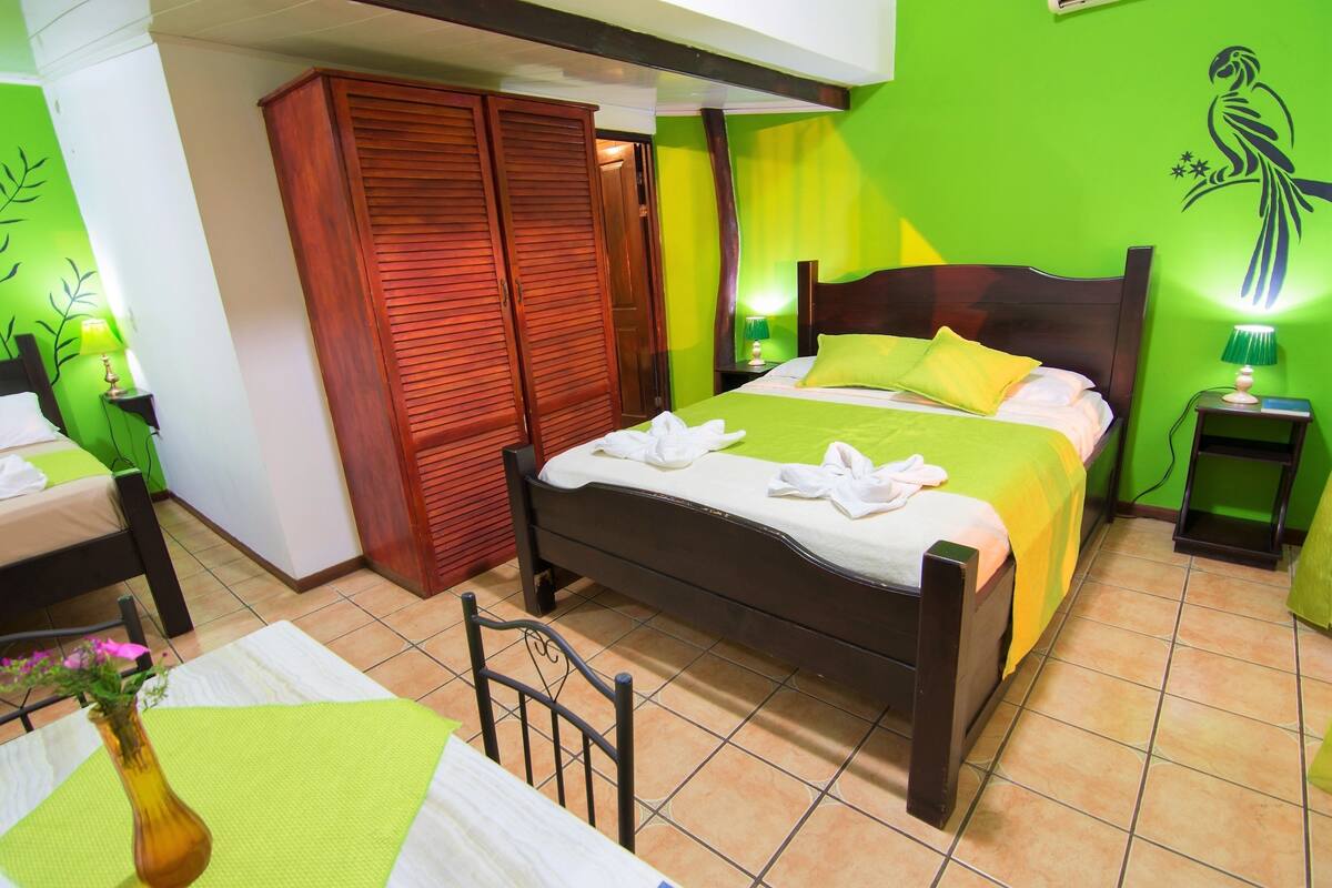 Un dormitorio con una cama, un armario de madera, una mesita de noche y una pared verde decorada con un mural de aves.