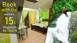 Quarto de hotel com uma cama, uma mesa e uma cadeira. Uma cascata e uma pessoa fazendo rapel ao fundo.
