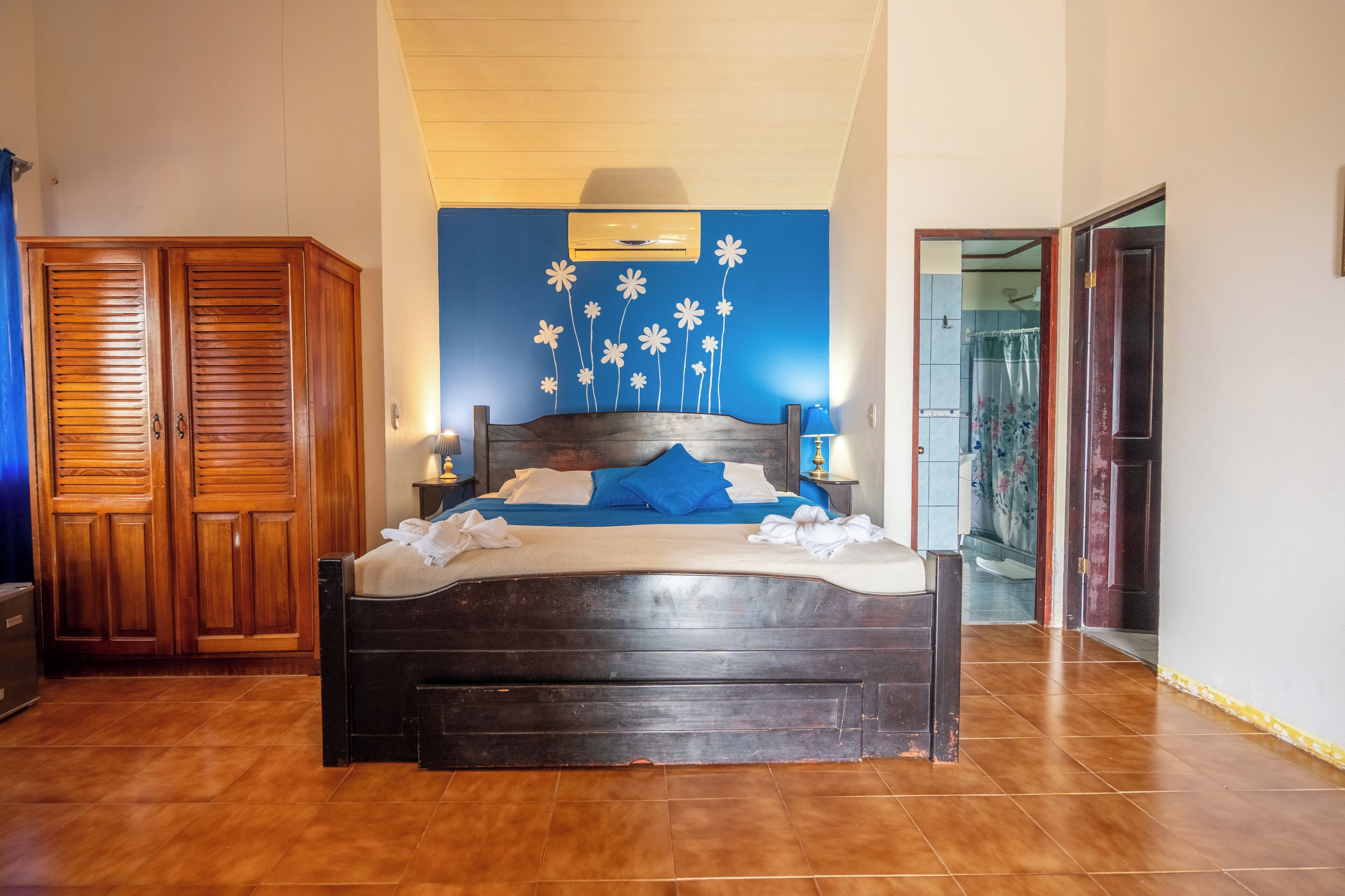 Quarto com cama de madeira, um guarda-roupa e banheiro visível por uma porta aberta.