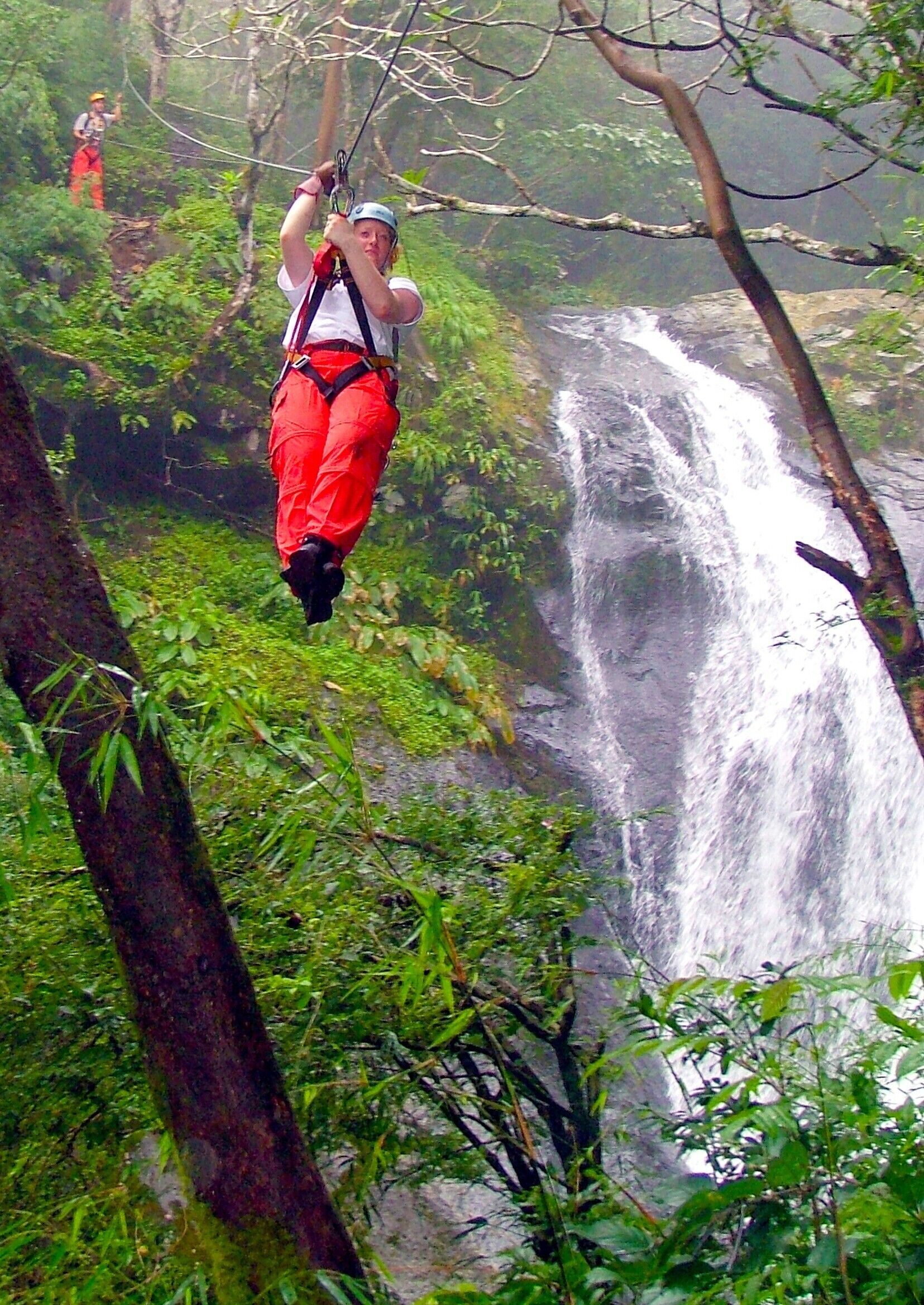 Una persona haciendo tirolesa por un bosque, con una cascada al fondo.