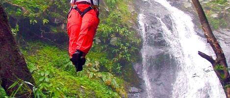 Una persona haciendo tirolesa por un bosque, con una cascada al fondo.