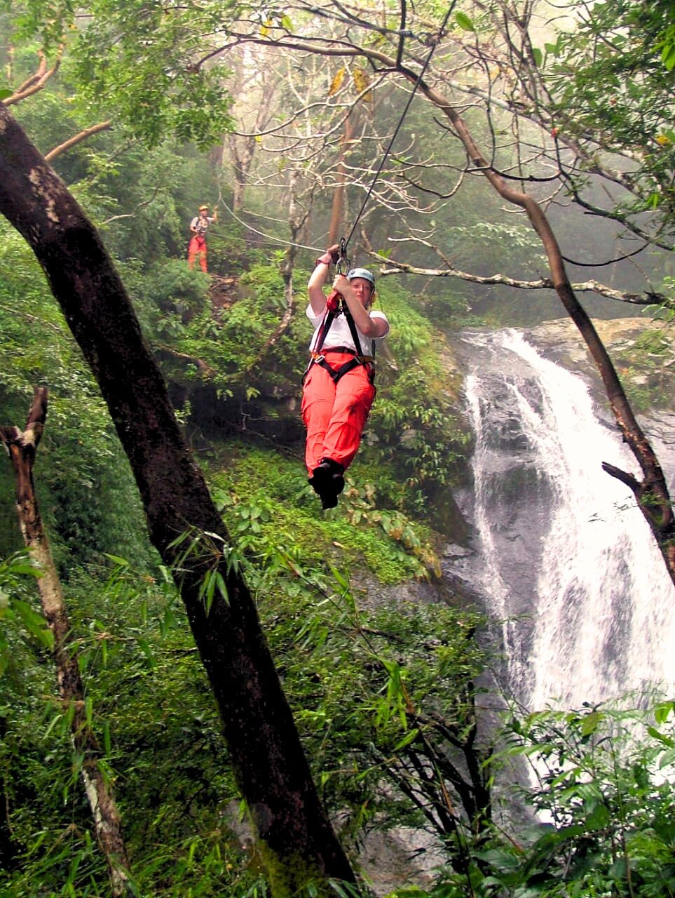 Une personne suspendue dans une forêt, avec une cascade en arrière-plan.