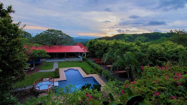 Um resort com piscina, um edifício com telhado vermelho e vegetação exuberante.